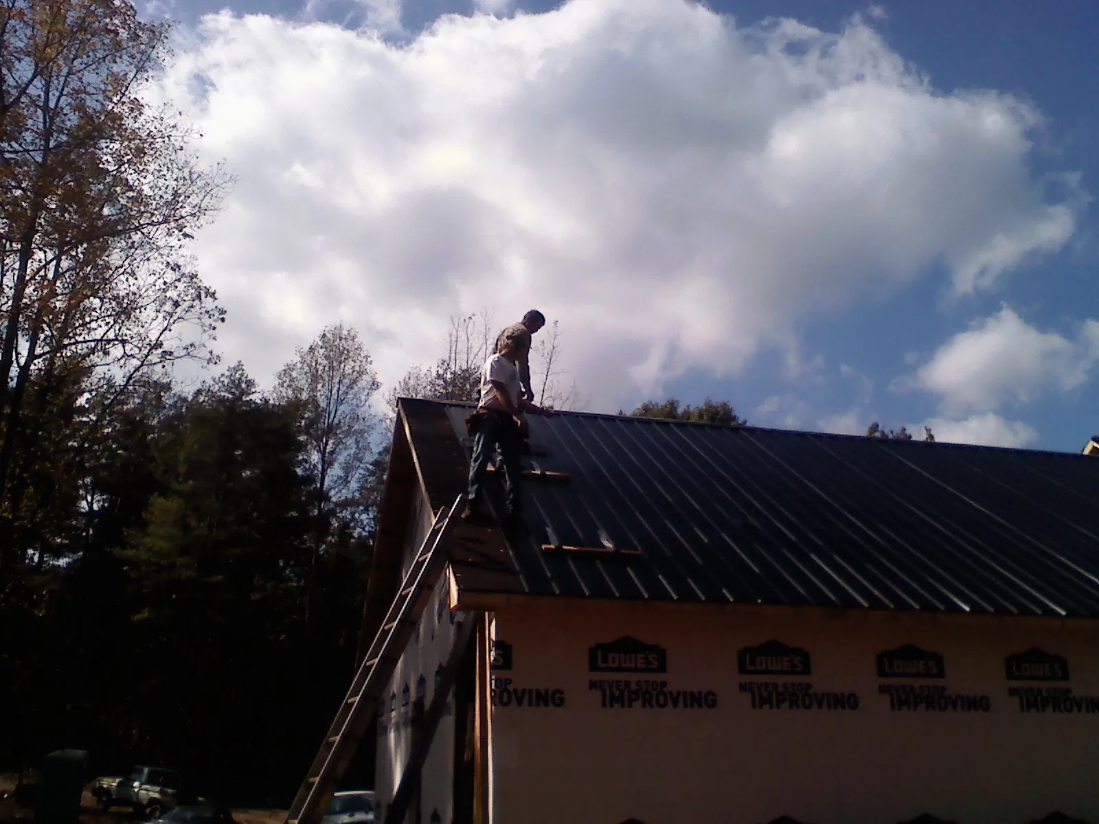 Roofer fastening dark metal panels high against a cloudy sky, from a Roof Inspection job in Lumberton